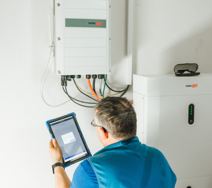 Elektrotechniker von Elektrotechnik Conzelmann bei der Inbetriebnahme eines PV-Wechselrichters mit Batteriespeicher und Monitoring per Table